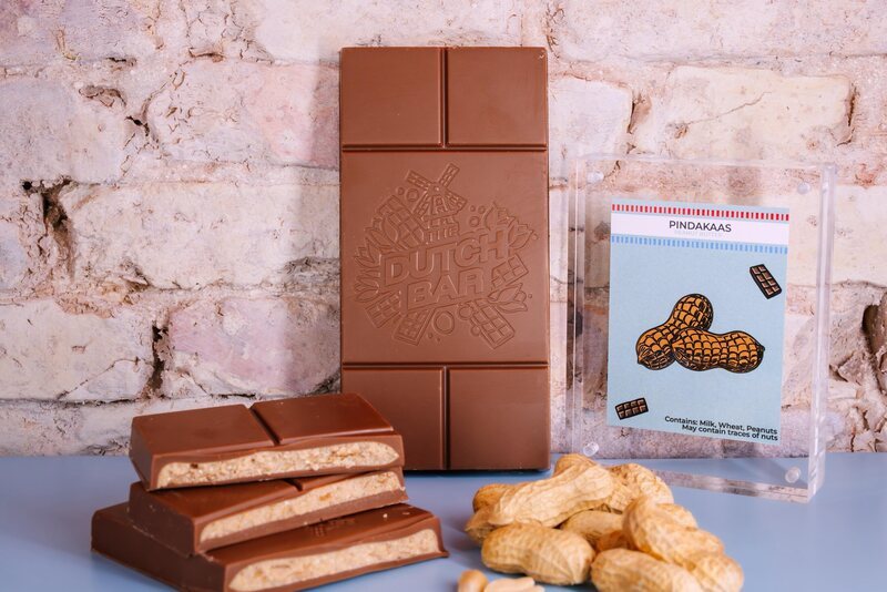 The peanut butter bar broken open to show its filling, next to peanuts and the blue flavour card