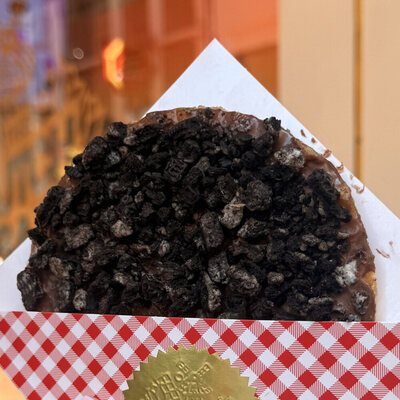A chocolate-dipped giant stroopwafel covered in dark Oreo cookie crumbs