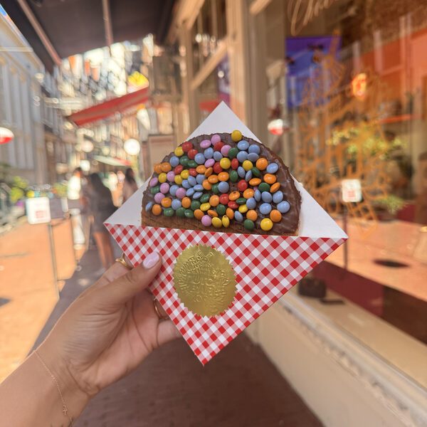 A smarties stroopwafel in its wrapper held up in the shopping street, with people walking past the shopfronts behind