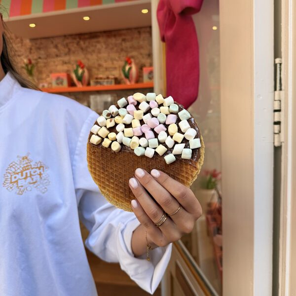 A member of staff in a white shirt with the gold Dutch Bar logo on the sleeve, holding out a marshmallow stroopwafel