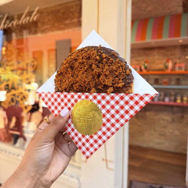 A giant stroopwafel covered in milk chocolate and crumbled Biscoff speculoos biscuit, held in a checked wrapper