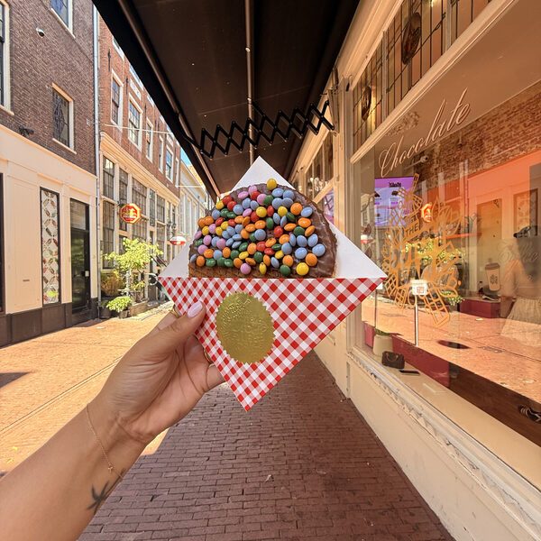 A smarties stroopwafel in its checked wrapper in front of the window, with the gold Dutch Bar windmill decal on the glass